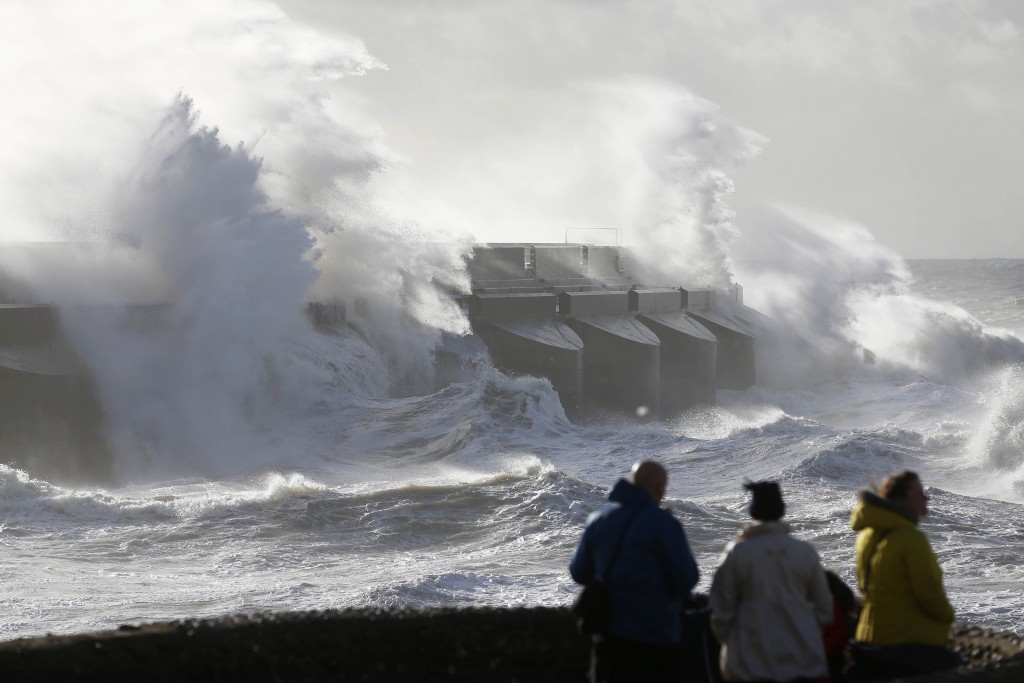 People watch the waves batter into the sea wall of a marina in Brighton, south England, Monday, Oct. 28, 2013. A major storm with hurricane force winds is lashing much of Britain, causing flooding and travel delays including the cancellation of roughly 130 flights at London's Heathrow Airport. Weather forecasters say it is one of the worst storms to hit Britain in years. (AP Photo/Sang Tan)