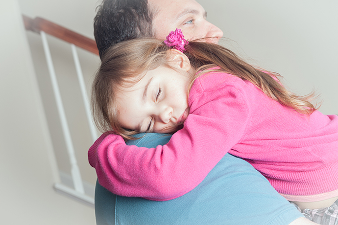 close up of litle girl preschool age sleeping in her dad's arms